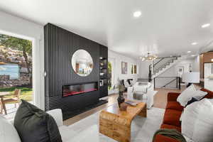 Living area featuring a glass covered fireplace, recessed lighting, a chandelier, stairway, and wood finished floors