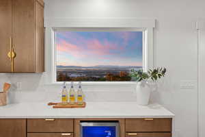 Bar area featuring light stone counters, brown cabinets, and beverage cooler
