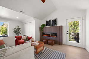 Living room with plenty of natural light, lofted ceiling, wood finished floors, a glass covered fireplace, and ceiling fan