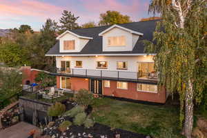 Back of house featuring a lawn, a shingled roof, brick siding, and a balcony