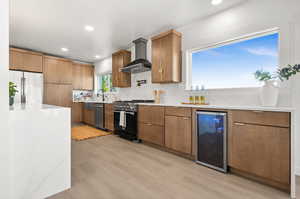 Kitchen featuring light stone countertops, appliances with stainless steel finishes, beverage cooler, recessed lighting, and wall chimney range hood