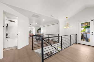 Corridor with light wood-style flooring, an upstairs landing, vaulted ceiling, a chandelier, and recessed lighting