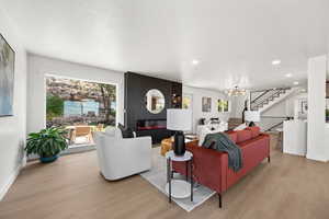 Living area with a large fireplace, a chandelier, light wood-type flooring, a textured ceiling, and stairway