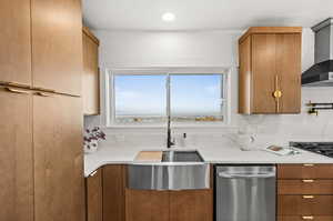 Kitchen with stainless steel dishwasher, light stone countertops, brown cabinetry, wall chimney exhaust hood, and a textured ceiling