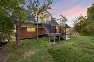 Back of house at dusk with stairway, a shingled roof, a yard, a patio area, and a deck