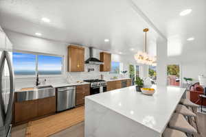 Kitchen with light stone counters, light wood-style floors, appliances with stainless steel finishes, brown cabinetry, and recessed lighting