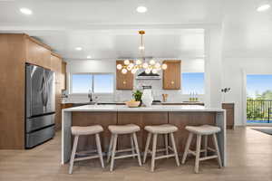 Kitchen featuring a kitchen breakfast bar, light stone counters, freestanding refrigerator, light wood-style floors, and recessed lighting