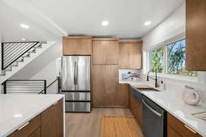 Kitchen featuring light wood-style flooring, appliances with stainless steel finishes, light stone counters, recessed lighting, and brown cabinets