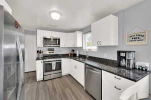 Kitchen featuring appliances with stainless steel finishes, a textured ceiling, light wood-style floors, dark stone countertops, and white cabinetry