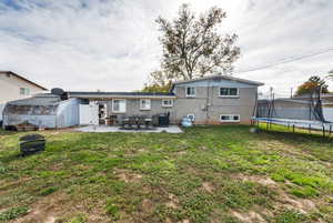 Back of house featuring a trampoline, a lawn, a patio area, and brick siding