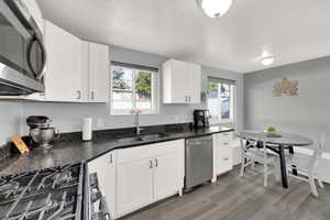 Kitchen featuring appliances with stainless steel finishes, white cabinets, light wood finished floors, a textured ceiling, and dark stone counters