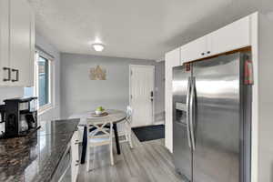 Kitchen with appliances with stainless steel finishes, a textured ceiling, light wood finished floors, white cabinets, and dark stone counters