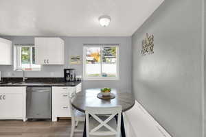 Kitchen with dishwasher, a textured ceiling, light wood-style floors, white cabinets, and dark stone counters