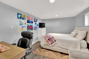 Bedroom with wood finished floors, recessed lighting, an office area, and a textured ceiling