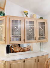 Kitchen with light brown cabinets, glass insert cabinets, and light countertops