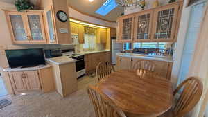 Kitchen with glass insert cabinets, light countertops, white appliances, a chandelier, and crown molding