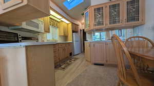 Kitchen featuring glass insert cabinets, a skylight, light countertops, white appliances, and a peninsula