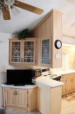 Kitchen with light brown cabinets, electric range, lofted ceiling, light countertops, and a peninsula