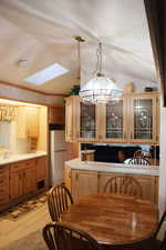 Kitchen featuring a skylight, light countertops, glass insert cabinets, decorative light fixtures, and freestanding refrigerator