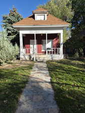 View of front facade featuring a porch, a front lawn, and roof with shingles
