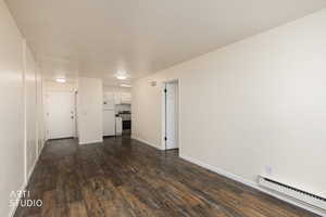 Unfurnished living room featuring a baseboard heating unit and dark wood finished floors
