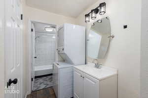 Bathroom featuring shower / tub combination, stacked washer and clothes dryer, vanity, dark wood finished floors, and a textured wall