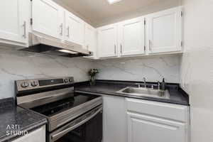 Kitchen with electric stove, backsplash, and white cabinets