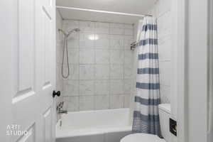 Full bathroom featuring shower / bathtub combination with curtain and toilet