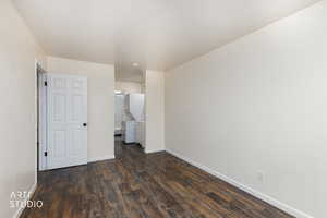 Unfurnished bedroom featuring dark wood-style floors, connected bathroom, and stacked washer and clothes dryer