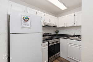 Kitchen featuring freestanding refrigerator, stainless steel electric stove, tasteful backsplash, white cabinetry, and a textured wall