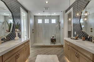 Full bathroom featuring tasteful backsplash, a walk in shower, two vanities, tile walls, and wood finish floors