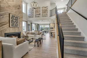 Living area featuring a chandelier, a towering ceiling, a fireplace, light wood-style floors, and stairway