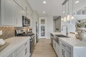 Kitchen with stainless steel appliances, light stone countertops, pendant lighting, light wood-type flooring, and backsplash