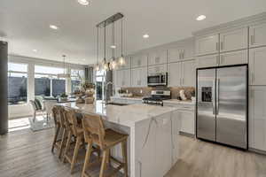 Kitchen with appliances with stainless steel finishes, a breakfast bar, light stone countertops, decorative light fixtures, and decorative backsplash