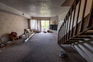 Unfurnished living room with a textured ceiling, carpet, and wallpapered walls