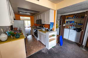 Kitchen featuring white cabinets, light countertops, gas range gas stove, finished concrete flooring, and washer and clothes dryer