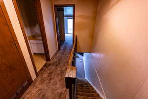 Corridor with an upstairs landing, dark colored carpet, and stairway