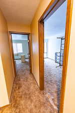Hallway with carpet floors, a textured ceiling, and a textured wall