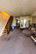 Living area featuring a textured ceiling, carpet flooring, and stairs
