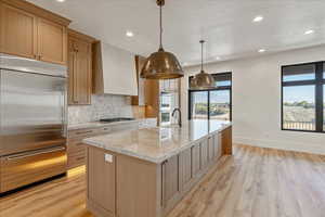 Kitchen with backsplash, built in refrigerator, light stone counters, recessed lighting, and light brown cabinetry