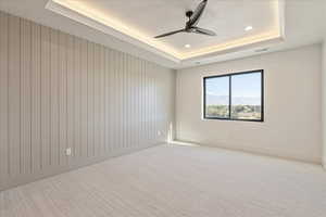 Unfurnished room with a raised ceiling, light colored carpet, a ceiling fan, recessed lighting, and a mountain view
