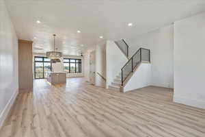 Unfurnished living room featuring recessed lighting, light wood-style floors, a chandelier, and stairway
