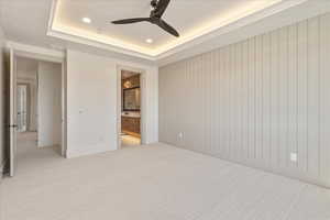 Unfurnished bedroom with a tray ceiling, light colored carpet, recessed lighting, a ceiling fan, and ensuite bathroom