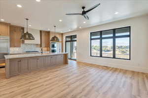 Kitchen with appliances with stainless steel finishes, a large island with sink, backsplash, hanging light fixtures, and light wood-type flooring