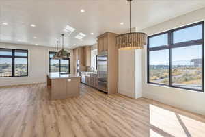 Kitchen with decorative light fixtures, a kitchen island, light stone counters, appliances with stainless steel finishes, and plenty of natural light