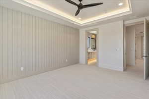 Unfurnished bedroom featuring a raised ceiling, light colored carpet, recessed lighting, ceiling fan, and ensuite bath