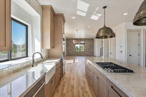 Kitchen featuring light wood finished floors, a skylight, brown cabinetry, appliances with stainless steel finishes, and decorative light fixtures