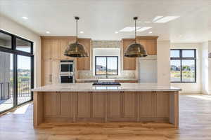 Kitchen with tasteful backsplash, light stone counters, a spacious island, light wood-type flooring, and recessed lighting