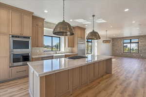 Kitchen featuring stainless steel appliances, light wood finished floors, light stone counters, a center island, and recessed lighting
