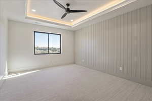 Empty room with a raised ceiling, light carpet, ceiling fan, and recessed lighting